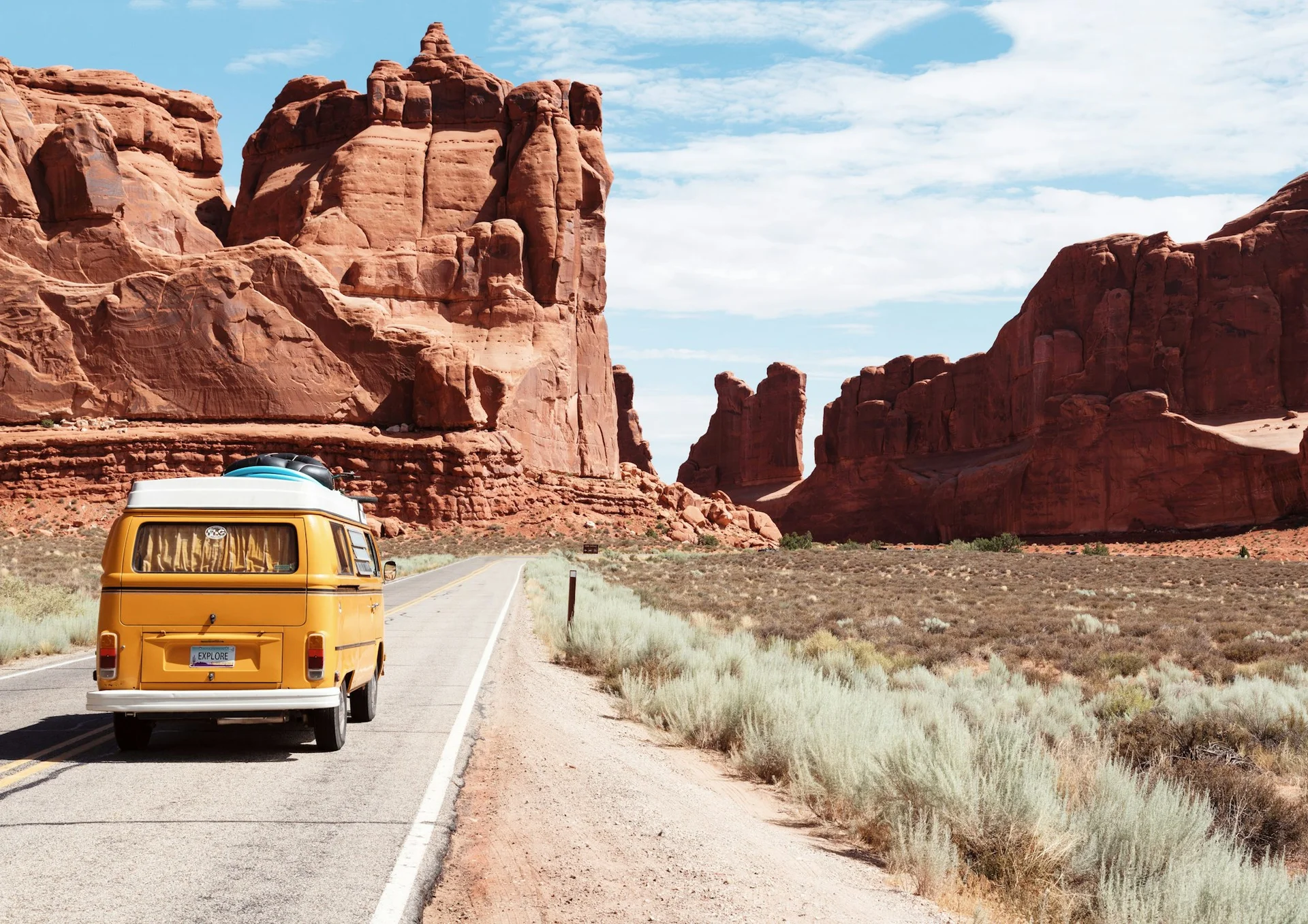 A camper van on an open desert highway between red rock cliffs